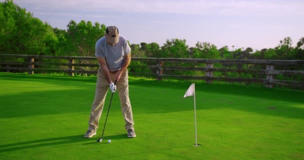 Knappe oudere golfer swingen en slaan golfbal op mooie baan bij zonsondergang. - Video