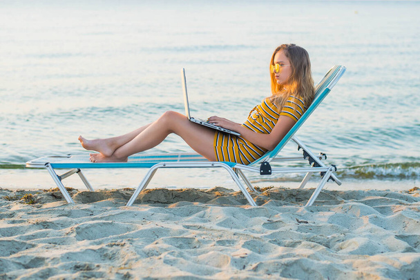 Young woman using laptop computer on a beach. Freelance work concept - Foto, afbeelding
