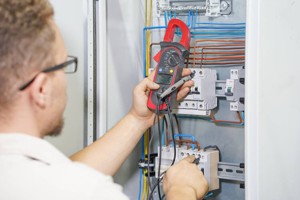 Multimeter is in hands of electrician on background of electrical automation cabinet. - Photo, Image