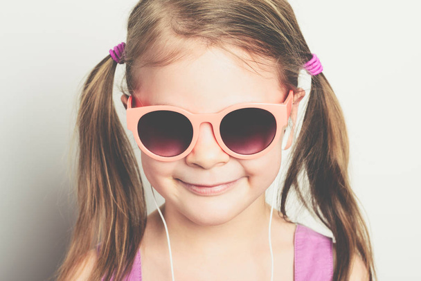 Güneş gözlüklü, kulaklıklı, gülen küçük mutlu kız. Stüdyo fotoğrafı. - Fotoğraf, Görsel