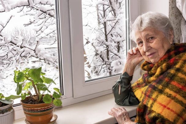 Stará osamělá žena sedící u okna v jeho domě. - Fotografie, Obrázek