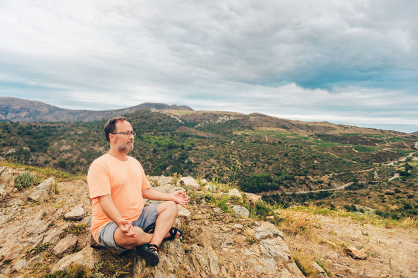 Outdoor portrait of handsome middle age man meditating, relaxing in the top of the mountain - 写真・画像