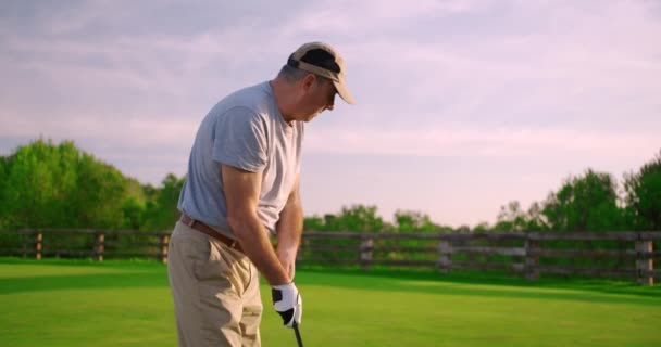 Knappe oudere golfer swingen en slaan golfbal op mooie baan bij zonsondergang. - Video