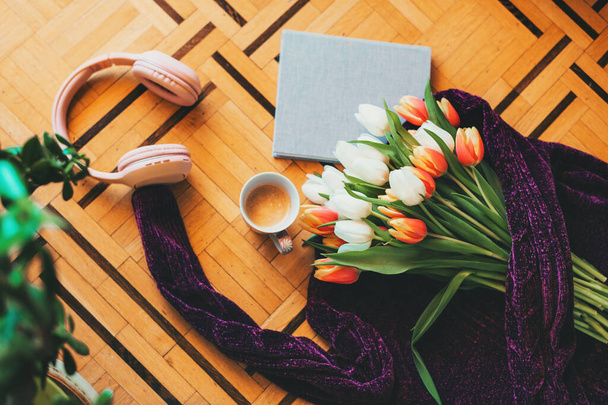 Spring still life, bouquet of tulips lying on purple pullover, small book with coffee cup and pink headphones - Fotoğraf, Görsel