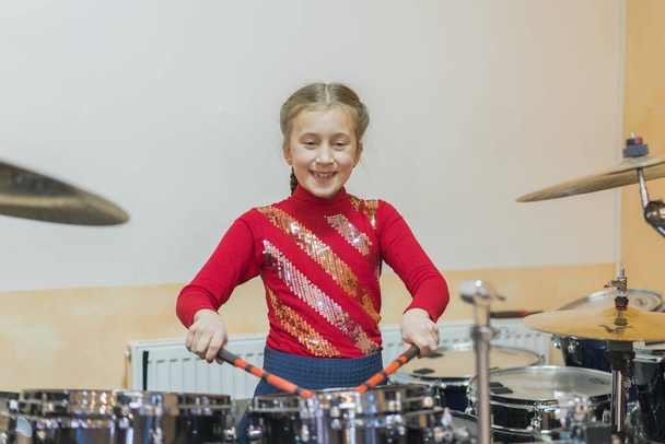 Μια έφηβη παίζει ντραμς. Έφηβη που διασκεδάζει παίζοντας drum sets στην τάξη μουσικής. - Φωτογραφία, εικόνα