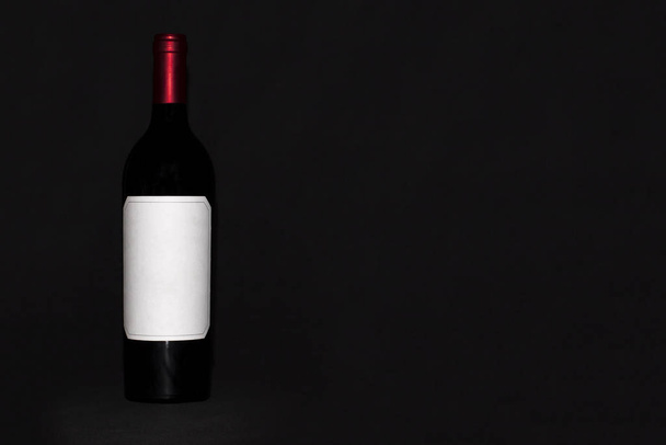 A full bottle of red wine with a white label on a dark background - Foto, Imagen