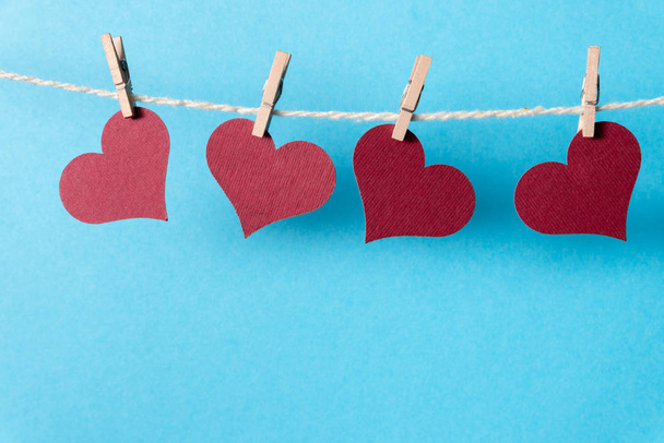 Μπορντό καρδιές κρέμονται σε ένα σχοινί με μικροσκοπικά μανταλάκια σε μπλε φόντο. - Φωτογραφία, εικόνα