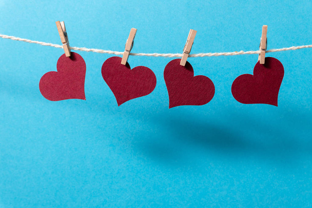 Бургундські серця звисають на мотузці з крихітними підкладками на синьому фоні.. - Фото, зображення