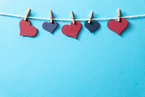 Πολύχρωμες καρδιές με σχοινί σε μικροσκοπικά μανταλάκια κρέμονται σε μπλε φόντο. - Φωτογραφία, εικόνα