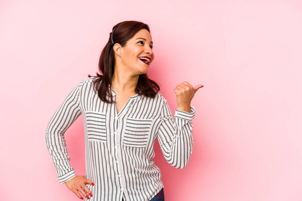 Middle age latin woman isolated on a pink background points with thumb finger away, laughing and carefree. - Photo, Image