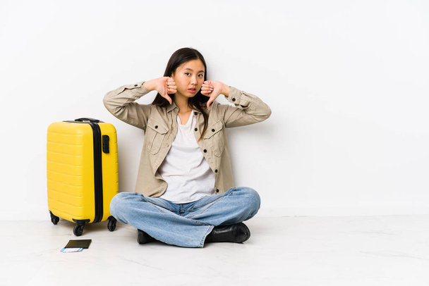 junge chinesische Reisende sitzt mit einer Bordkarte, die Daumen nach unten zeigt und ihre Abneigung ausdrückt. - Foto, Bild