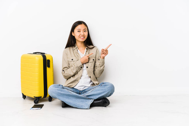 Молодая китайская путешественница, сидящая с посадочными талонами, шокирована, указывая указательными пальцами на копировальное пространство.
. - Фото, изображение