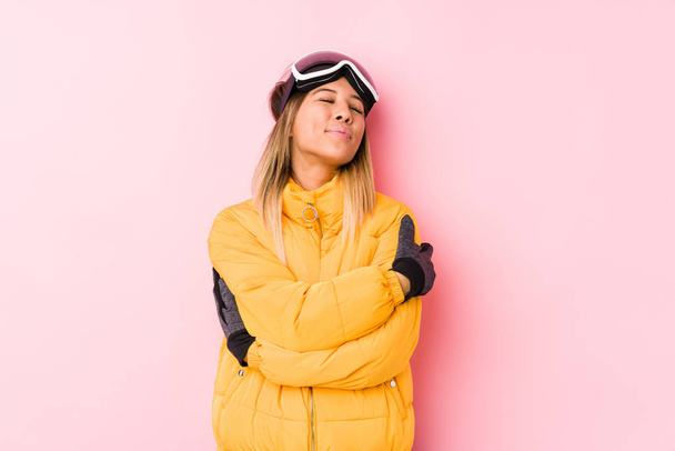 Młoda biała kobieta ubrana w szaty narciarskie w różowym tle przytula, uśmiechając się beztrosko i szczęśliwie. - Zdjęcie, obraz