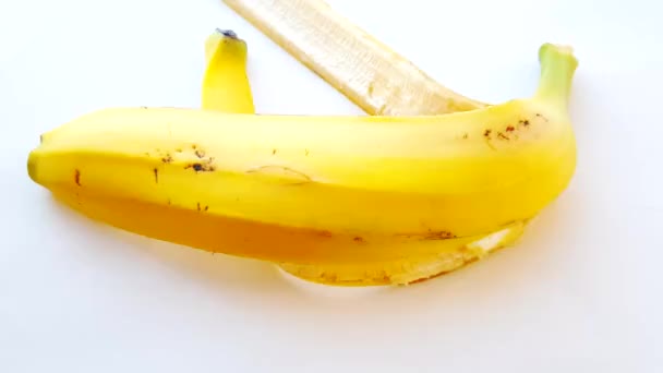 Cáscara de plátano sobre un fondo blanco con luz solar brillante, la mano de una mujer pone la cáscara sobre la mesa
 - Metraje, vídeo
