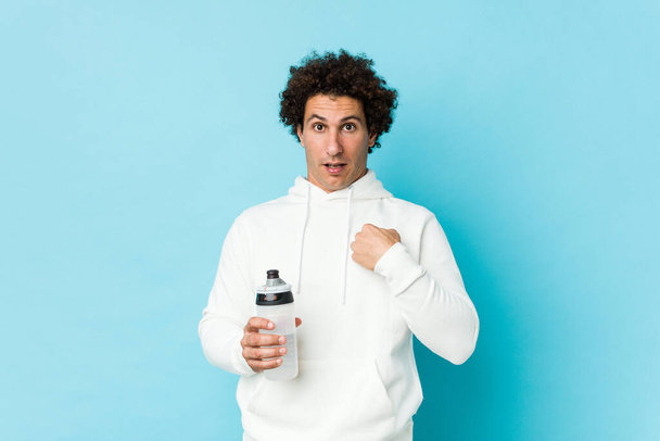 Sport man holding a water bottle surprised pointing at himself, smiling broadly. - Foto, afbeelding