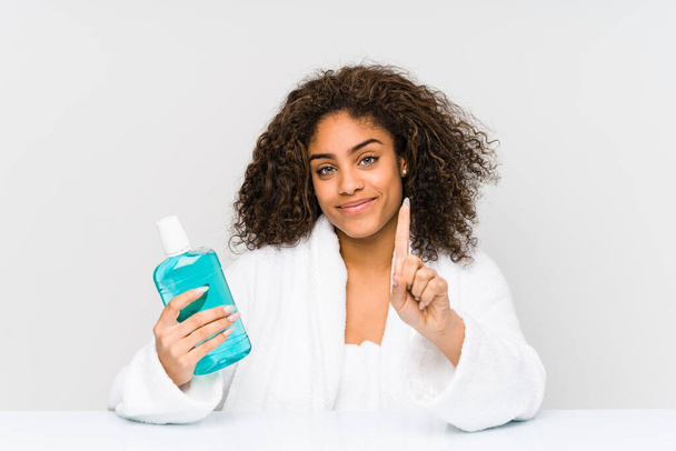 Young african american woman holding a mouth wash showing number one with finger. - Foto, Imagem