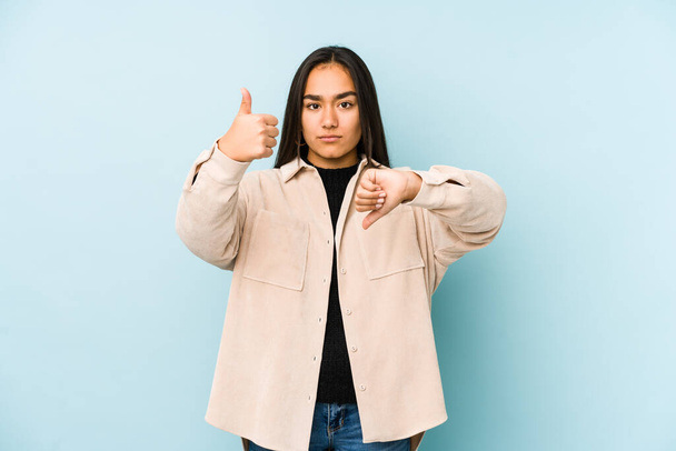 Young woman isolated on a blue background showing thumbs up and thumbs down, difficult choose concept - Photo, Image