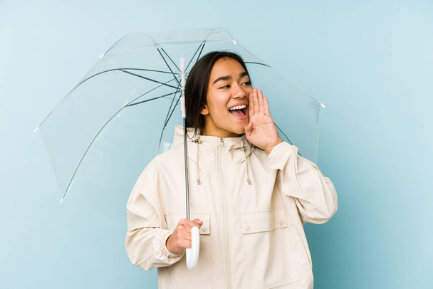 Joven mujer asiática sosteniendo un paraguas gritando y sosteniendo la palma cerca de la boca abierta
. - Foto, Imagen
