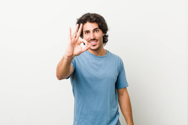 Young handsome man against a white background cheerful and confident showing ok gesture. - Photo, Image