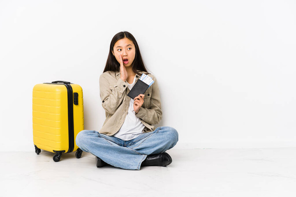 Joven viajera china sentada sosteniendo una tarjeta de embarque está diciendo una noticia secreta de frenado caliente y mirando a un lado
 - Foto, Imagen