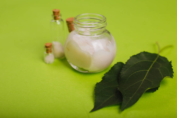 Cosméticos ecológicos. Un frasco de crema blanca y las hojas del árbol sobre un fondo verde. Cuidado de la piel. Frascos de sal marina
 - Foto, Imagen