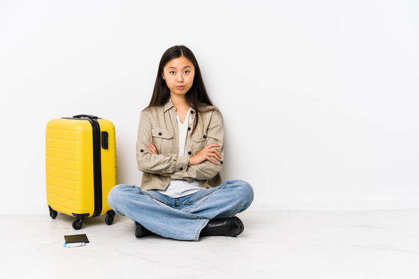Joven viajera china sentada sosteniendo una tarjeta de embarque infeliz mirando en cámara con expresión sarcástica
. - Foto, imagen