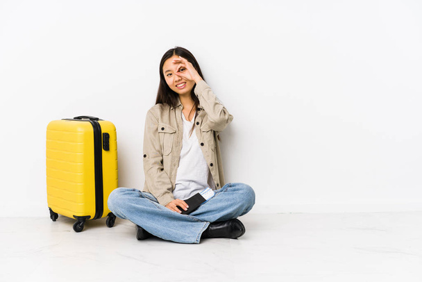 Joven viajera china sentada sosteniendo una tarjeta de embarque emocionada manteniendo un buen gesto a la vista
. - Foto, Imagen