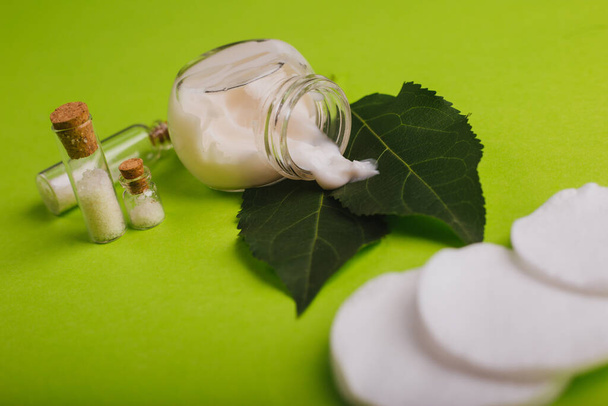 Cosméticos ecológicos. Un frasco de crema blanca y las hojas del árbol sobre un fondo verde. Cuidado de la piel. Frascos de sal marina
 - Foto, imagen