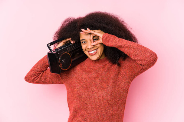 Joven afro mujer sosteniendo un cassete aislado excitado mantener el gesto ok en el ojo
. - Foto, imagen