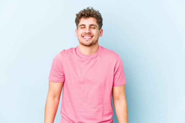 Young blond curly hair caucasian man isolated laughs and closes eyes, feels relaxed and happy. - Photo, Image