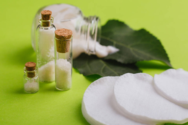 Eco cosmetics. A jar of white cream and the leaves of the tree on a green background. Skin care. Sea salt jars - Photo, Image