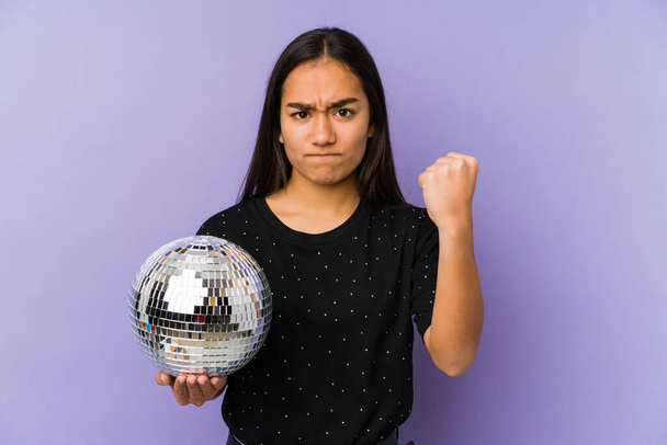 Young asian woman holding a ball party isolated showing fist to camera, aggressive facial expression. - Фото, зображення