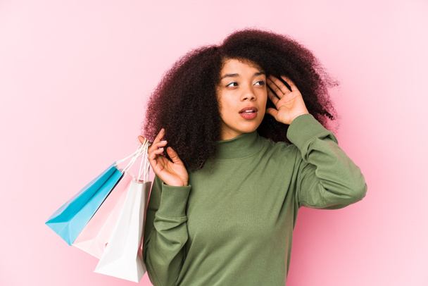 Young afro woman shopping isolated Young afro woman buying isolaYoung afro woman holding a roses isolated trying to listening a gossip. - Photo, Image