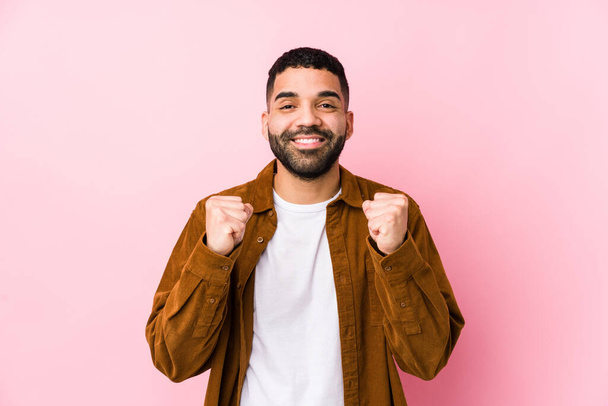 Молодий латинський чоловік на фоні рожевого ізольованого піднятого кулака, відчуває себе щасливим і успішним. концепція Перемоги
. - Фото, зображення