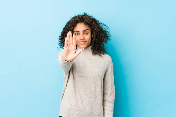 jonge afrikaanse amerikaanse krullend haar vrouw staande met uitgestrekte hand tonen stop teken, voorkomen dat u. - Foto, afbeelding