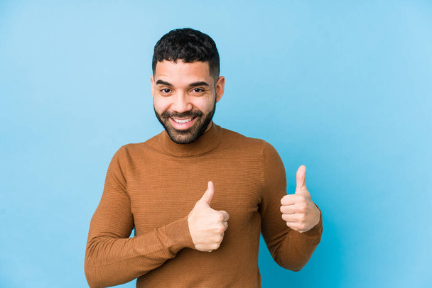 Young latin man against a blue  background isolated raising both thumbs up, smiling and confident. - Fotografie, Obrázek