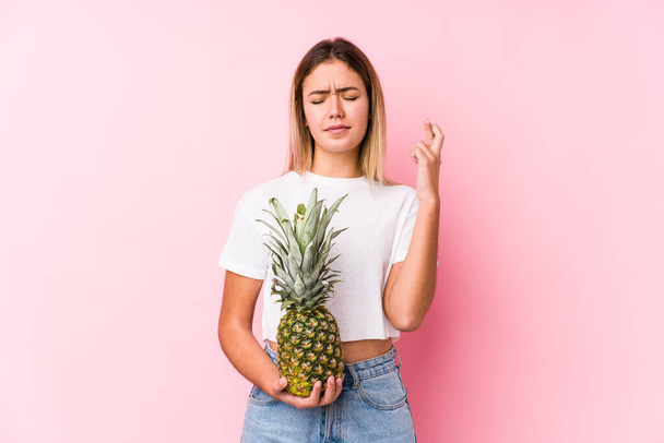 Young caucasian woman holding a pineapple crossing fingers for having luck - Photo, Image