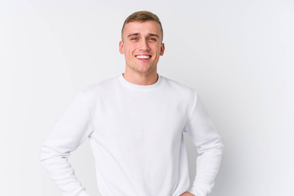 Young caucasian man on white background confident keeping hands on hips. - 写真・画像