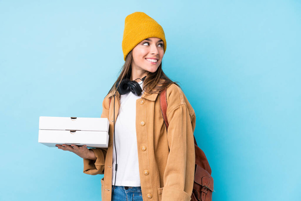 Jeune femme caucasienne tenant des pizzas isolées regarde de côté souriant, gai et agréable. - Photo, image