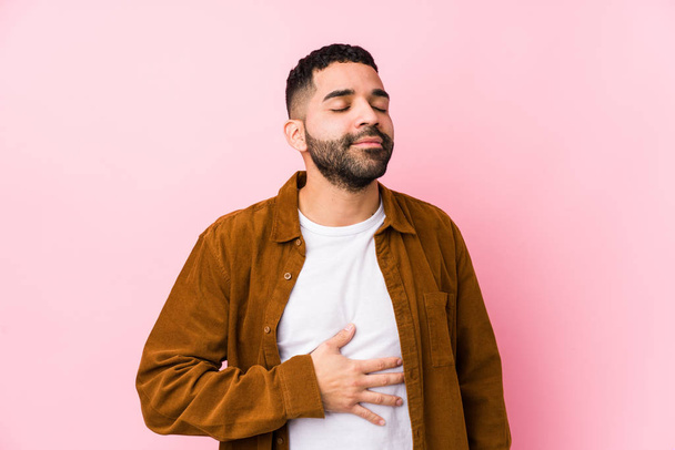 Young latin man against a pink background isolated touches tummy, smiles gently, eating and satisfaction concept. - Foto, immagini