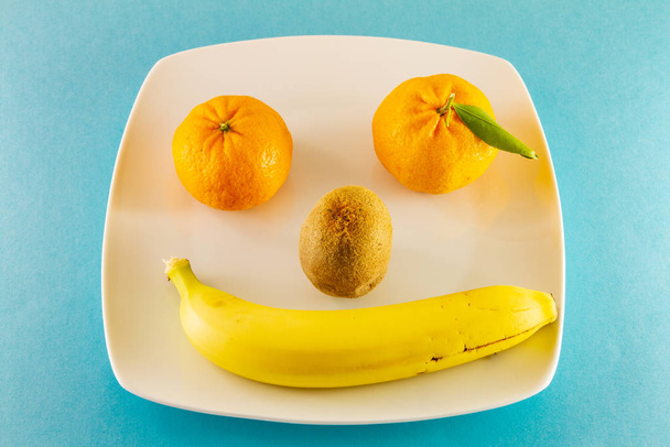 Tangerines kivi és egy banán fehér tálcán, mosolygós emberként. - Fotó, kép