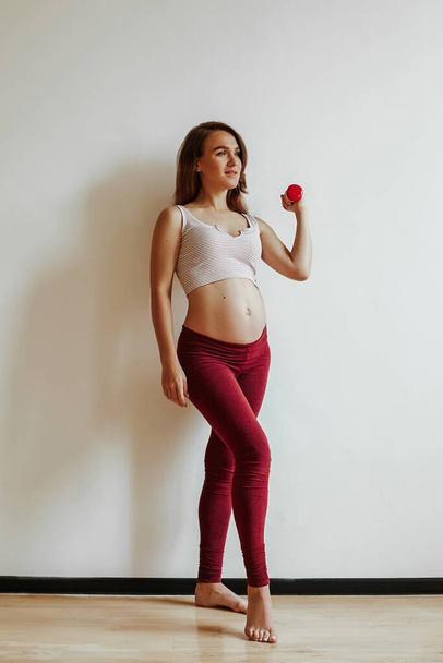 A brown-haired girl is engaged in fitness before childbirth. Sports lifestyle. Lift the dumbbell with your hand. - Foto, imagen