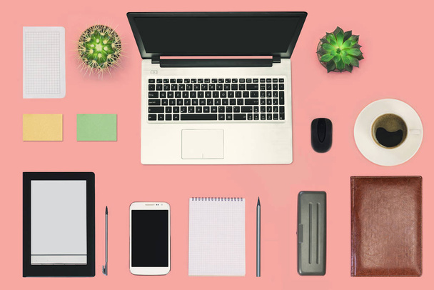 Moderne werkruimte, technologisch werkbureau met laptop, koffiebeker, kantoorbenodigdheden, e-book en smartphone op roze pastelachtergrond met kopieerruimte. Bovenaanzicht. Vlakke plaat. - Foto, afbeelding