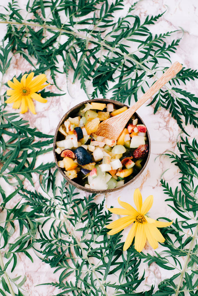 terveellistä hedelmäsalaattia lautasella kookospähkinän kuoret pöydällä trooppisia lehtiä. kasvisruoka
 - Valokuva, kuva