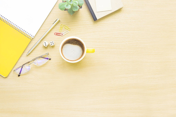 Mesa de escritorio de oficina de madera con cuaderno, vasos, planta, taza amarilla de café con leche y otros suministros de oficina. Vista superior con espacio de copia, plano
. - Foto, imagen