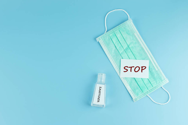 Protective face mask and sanitizer gel dispenser  on blue backgr - Photo, Image