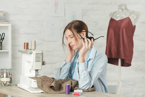 Sleepy, frustrated, exhausted seamstress with headache on her work desk. Small business or self-employed problems. Deadline or overwork concept, bored or getting tired at work in creative industry. - Fotoğraf, Görsel