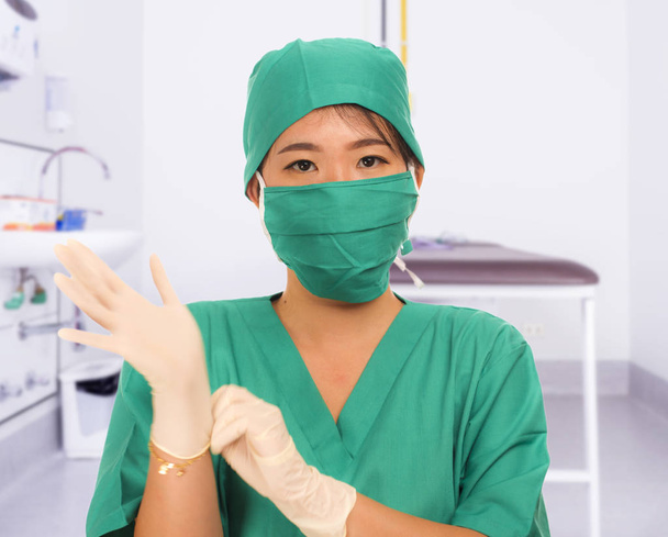 young beautiful and happy Asian medicine doctor or chief hospital nurse in green scrubs and surgey hat and mask putting  latex gloves - Photo, Image