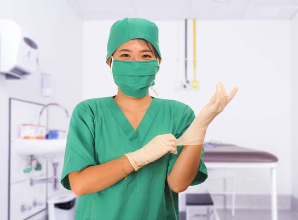 young beautiful and happy Asian medicine doctor or chief hospital nurse in green scrubs and surgey hat and mask putting  latex gloves - Foto, immagini
