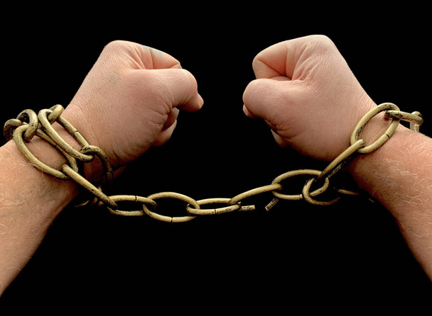 Men's hands break the chain, on a black background. The man is chained, his hands are tied. The concept of freedom, slavery. - Photo, Image